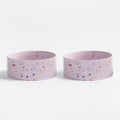 Two pink ceramic dog bowls with multicoloured speckles on a white background