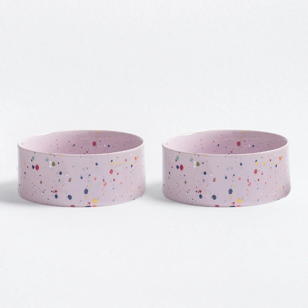 Two pink ceramic dog bowls with multicoloured speckles on a white background
