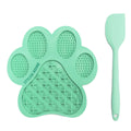 Mint green paw-shaped silicone lick mat and spatula on a white background