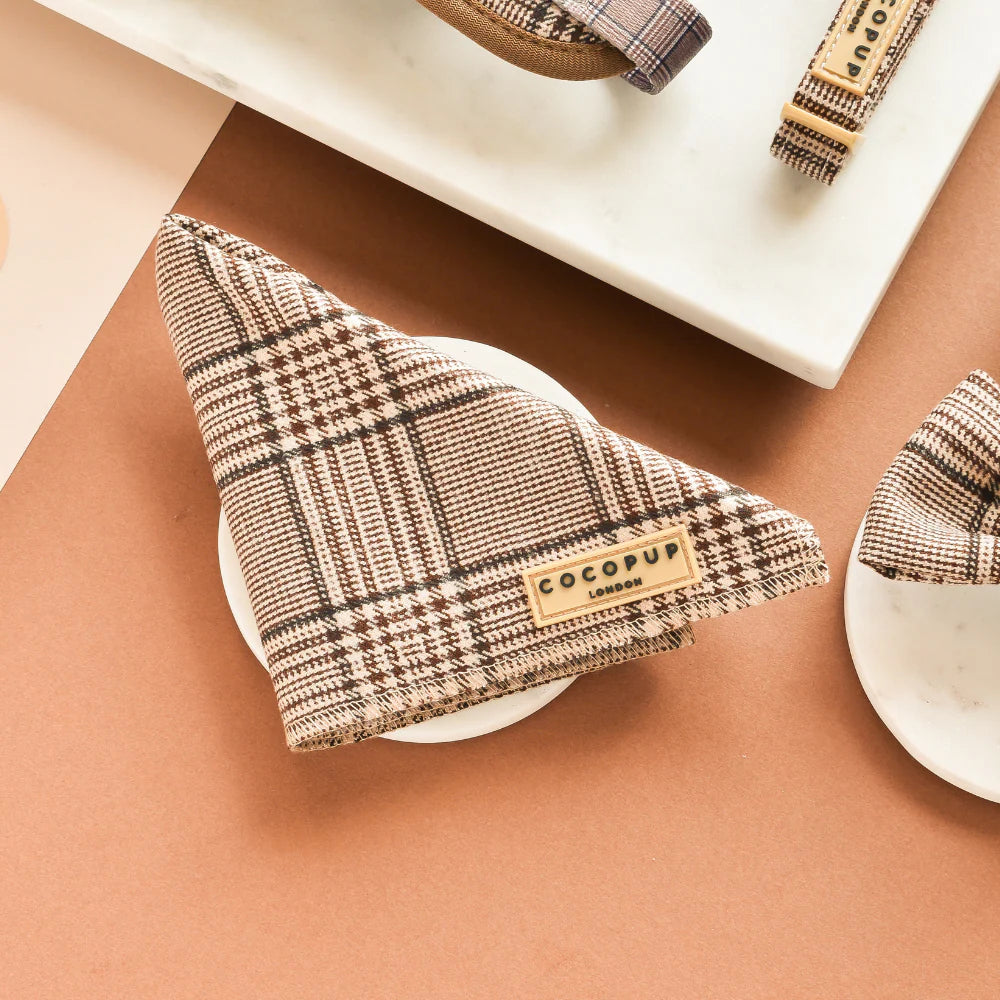 Plaid-patterned dog bandana with 'Cocopup' branding on a brown surface.